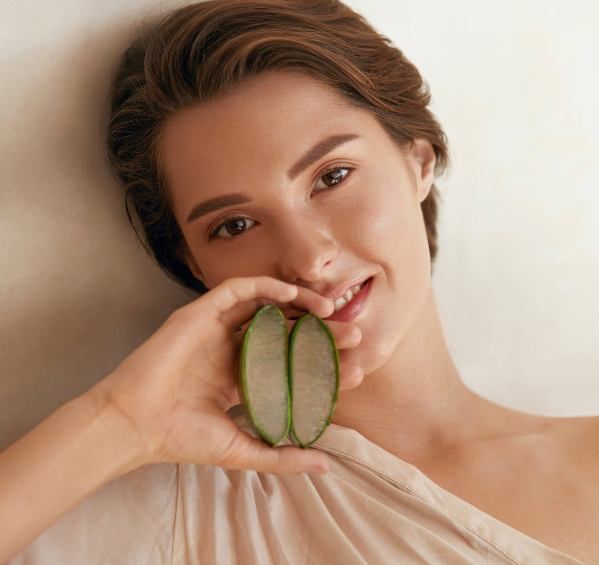 Frau hält ein aufgeschnittenes Aloe-Vera-Blatt vor das Gesicht