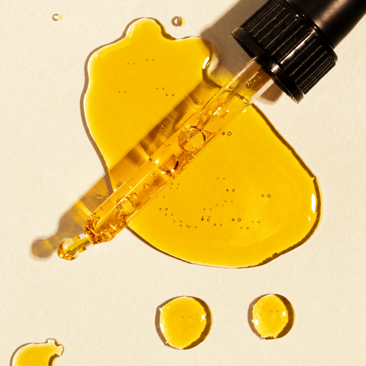 Goldenes Pflanzenöl mit Glaspipette auf hellem Naturpapier