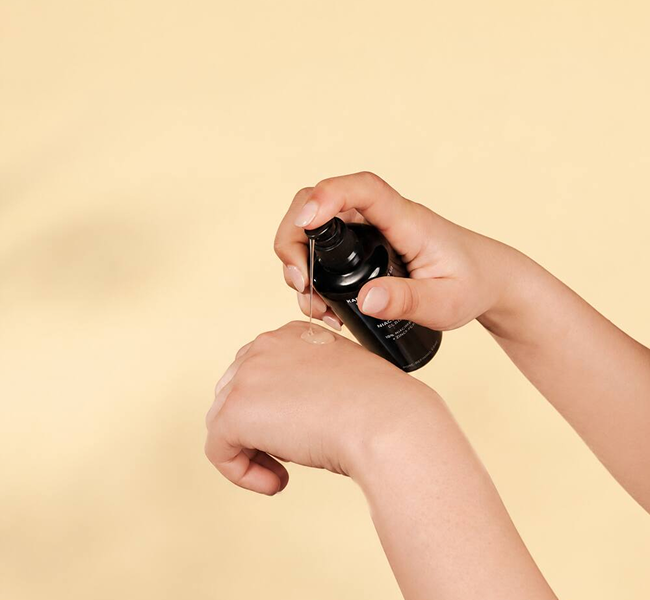 BIO NIACINAMID SERUM wird auf den Handrücken dosiert, vor warmgelbem Hintergrund