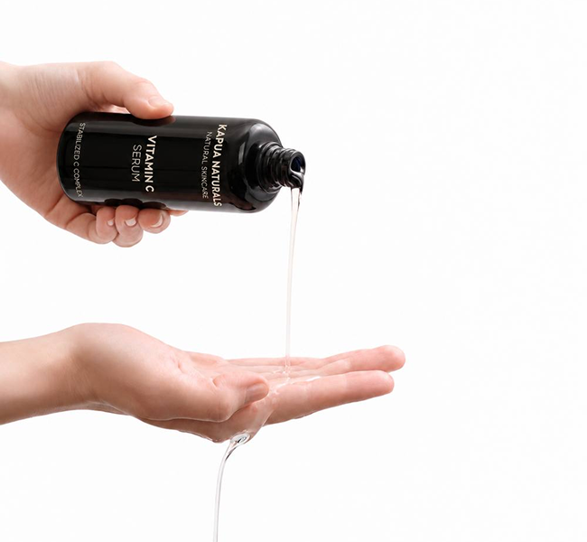 Bio Vitamin C Serum fließt aus der geöffneten Flasche in eine Handfläche vor weißem Hintergrund
